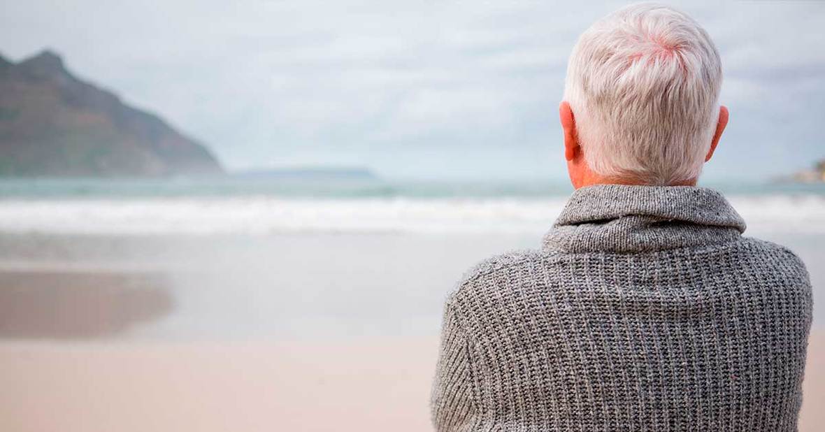 Hombre mayor viudo en la playa mirando el mar