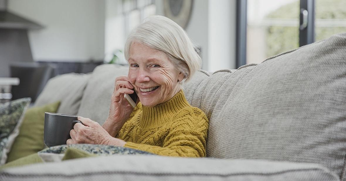 Mujer mayor hablando por teléfono sentada en el sofá de su casa