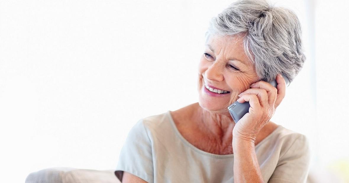 Mujer mayor, sentada en el sofá de su casa, hablando por teléfono