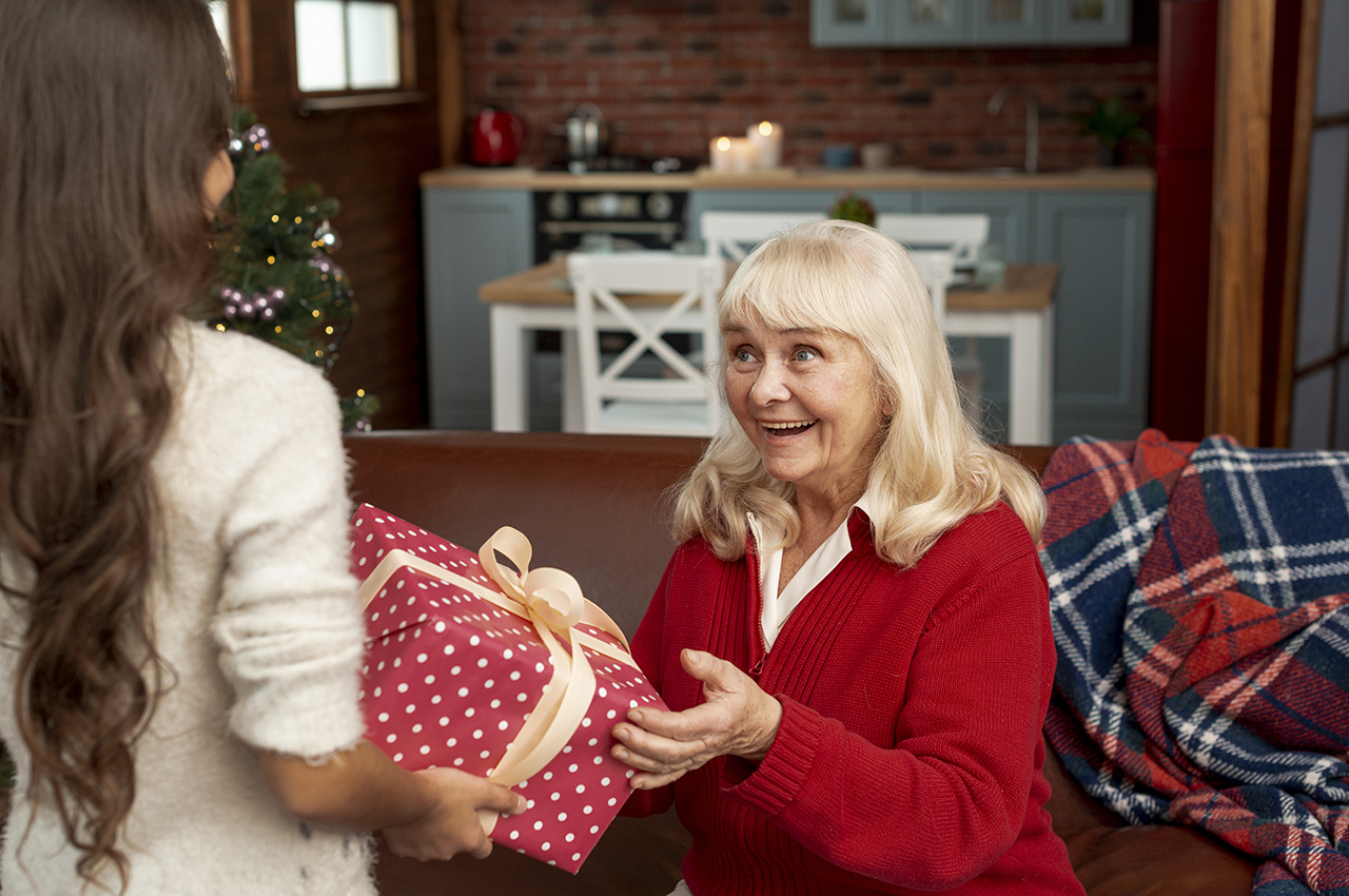 Una abuela recibe un regalo envuelto con un lazo de manos de su nieta.