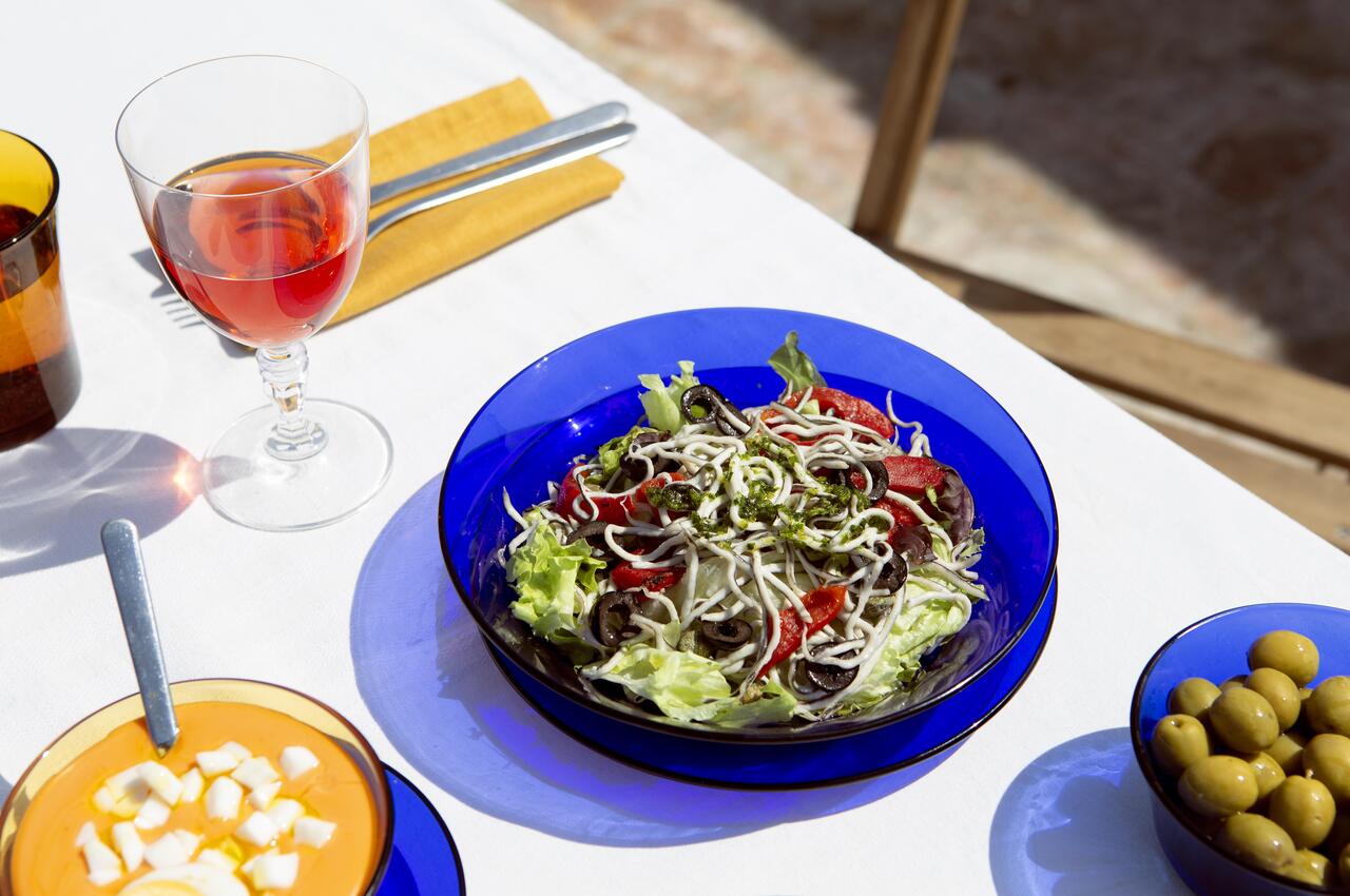 Una ensalada con gulas, un plato con salmorejo y huevo cocido, y un cuenco con aceitunas manzanilla.