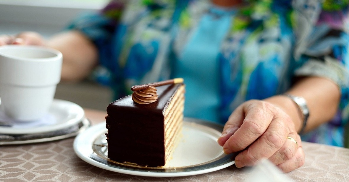 Persona mayor sin dientes comiendo un trozo de pastel de chocolate de postre