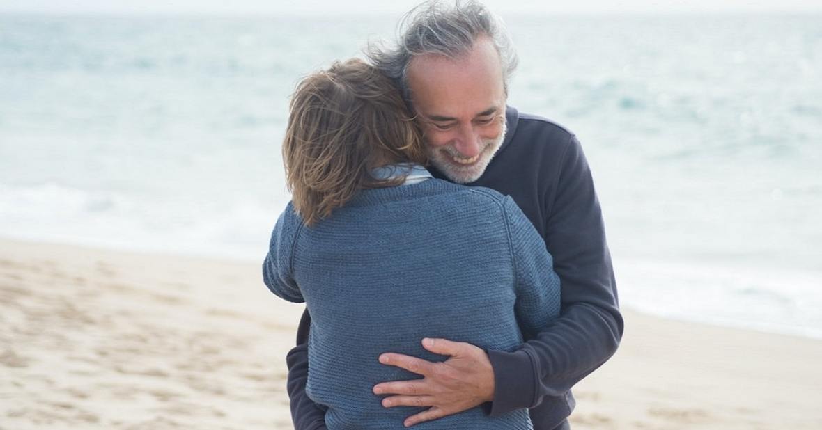 Hombre mayor y mujer abrazados en la orilla de una playa