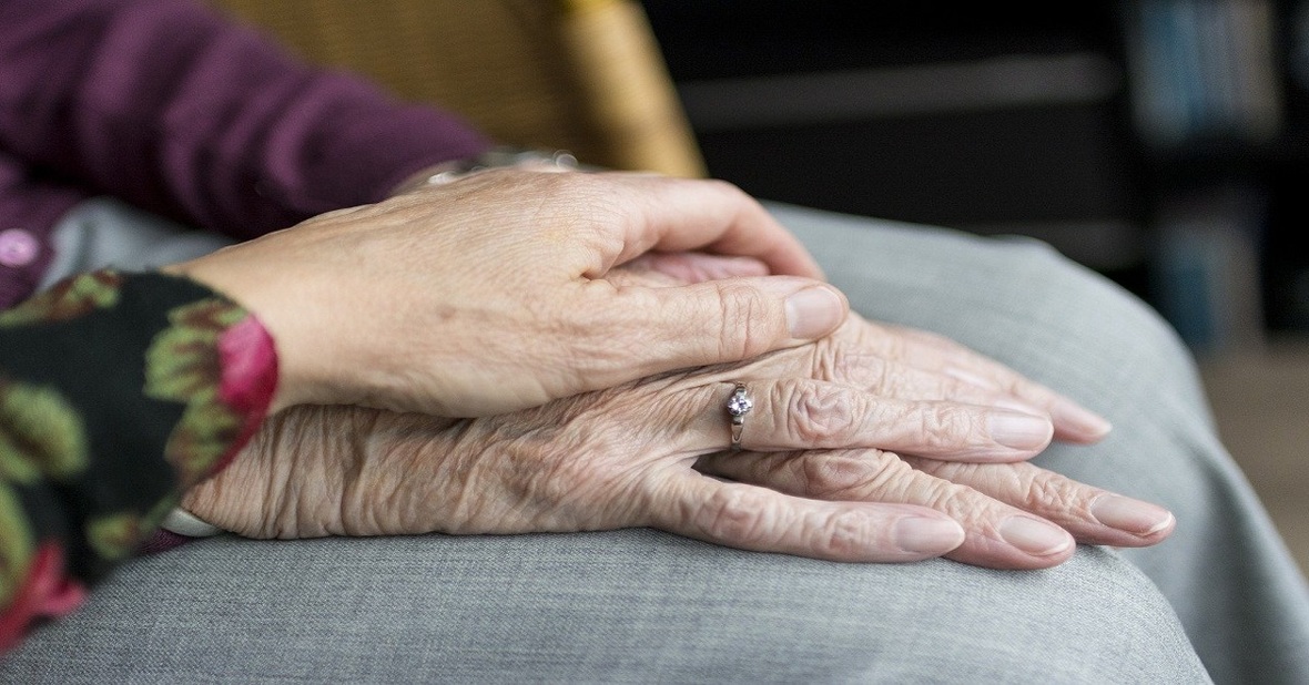 Joven poniendo la mano sobre la de una mujer mayor en etapa de envejecimiento como muestra de cariño