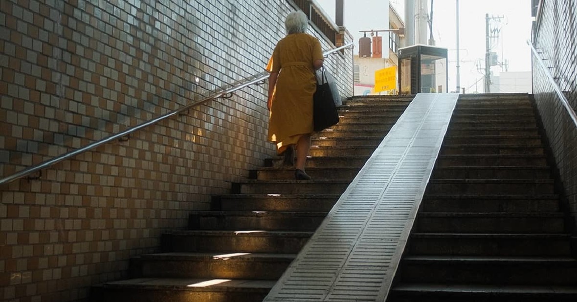 Mujer mayor subiendo unas escaleras llevando bolsas en las manos, una de las causas más frecuentes de rotura de cadera en personas mayores.