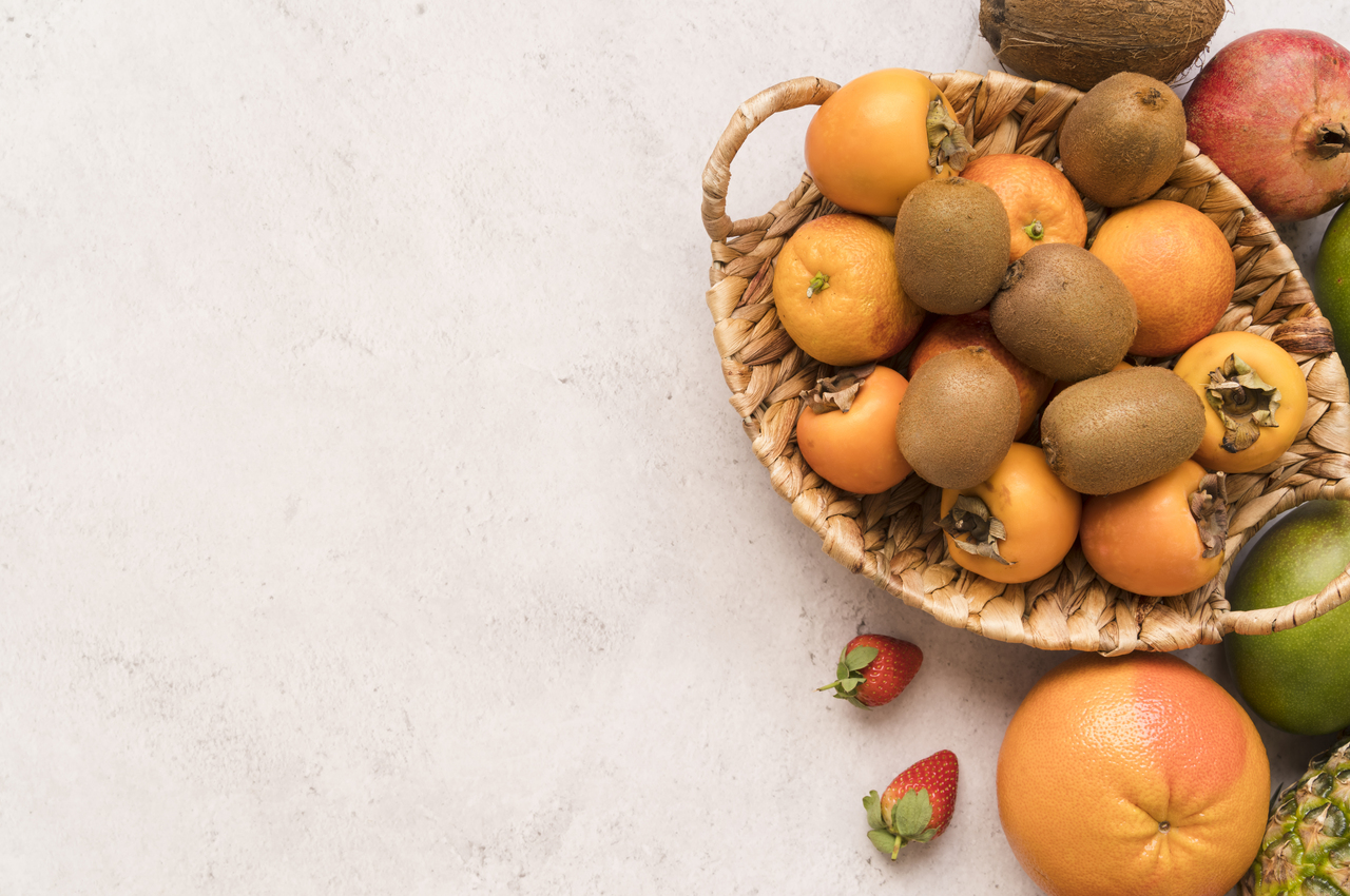Una cesta con frutas de temporada otoñal: kiwi, naranja, caqui...