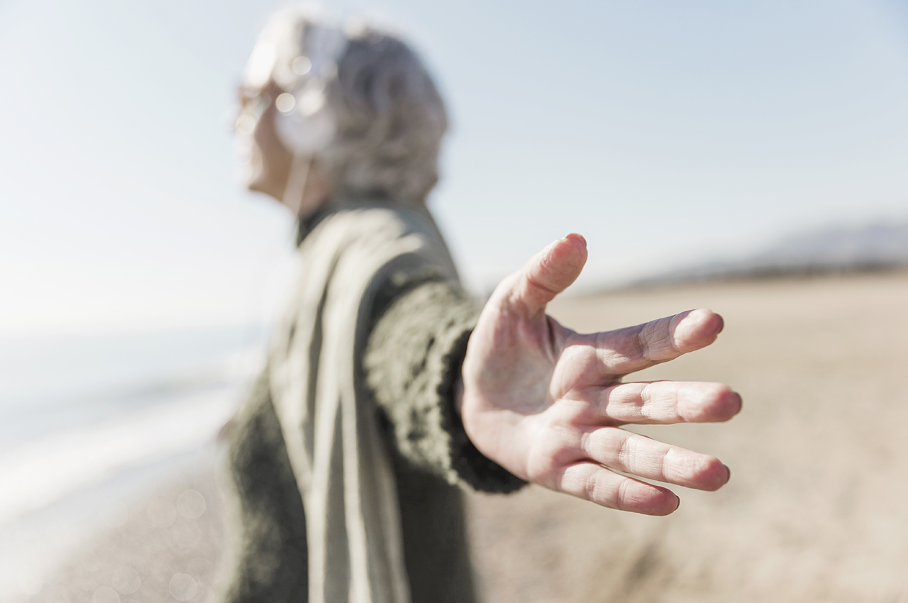 Una mujer mayor de perfil mira hacia la playa. Su expresión transmite tranquilidad y paz interior.