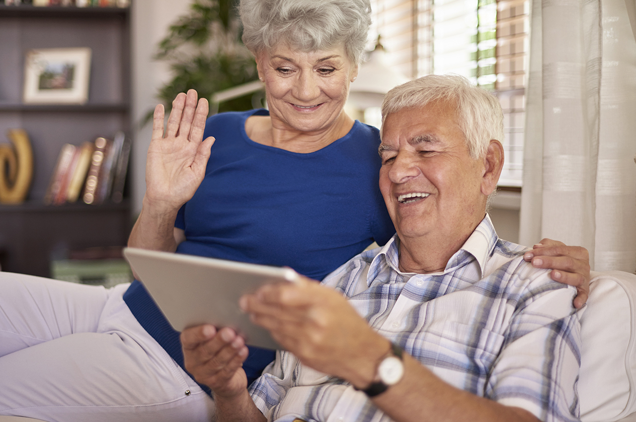 Una pareja de personas mayores hacen una videollamada desde su tablet.