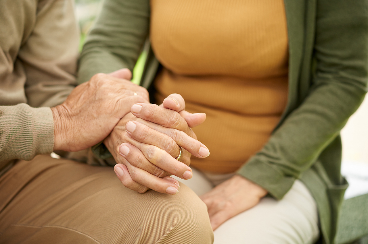 Dos personas mayores entrelazando las manos. La que está en la izquierda, pone su mano encima de las que están entrelazadas.