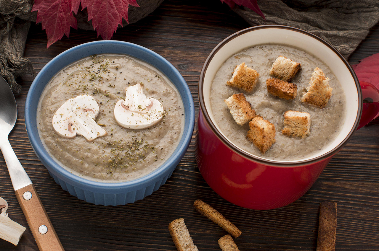 Un bol y una taza con crema de calabaza. El bol está decorado con dos láminas de champiñón, mientras que a la taza la coronan un par de picatostes.