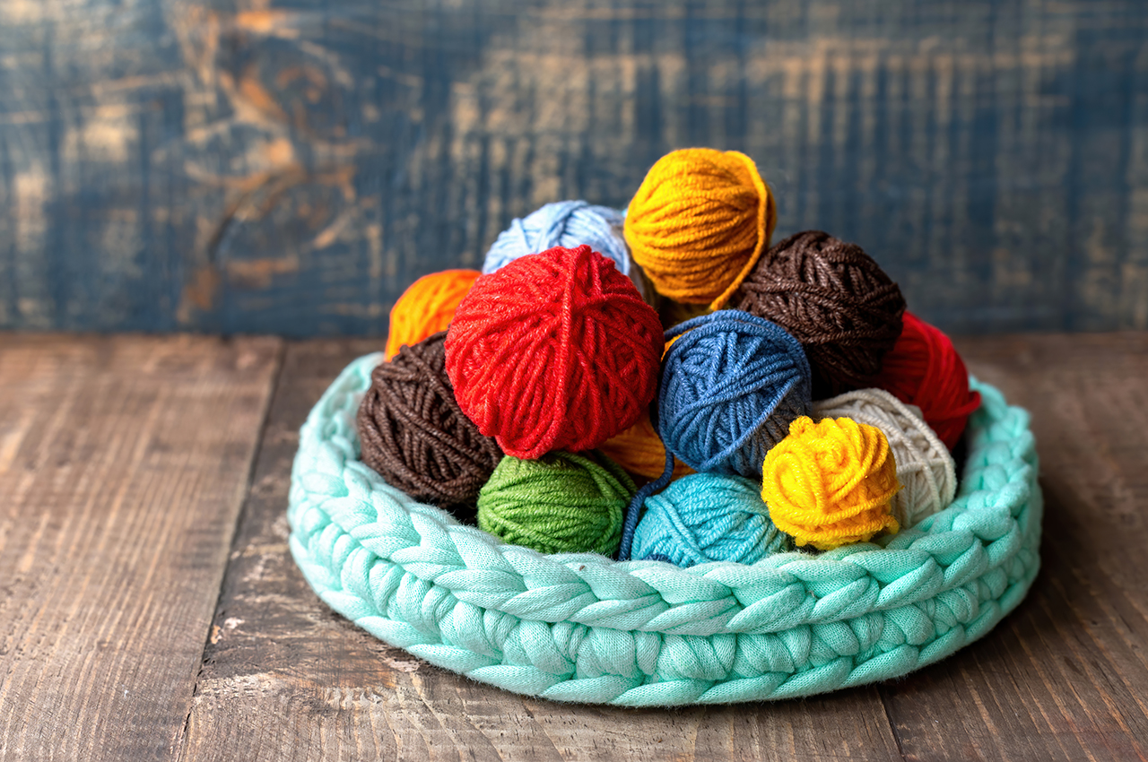 Cesta llena de ovillos de lana de distintos colores y tamaños.