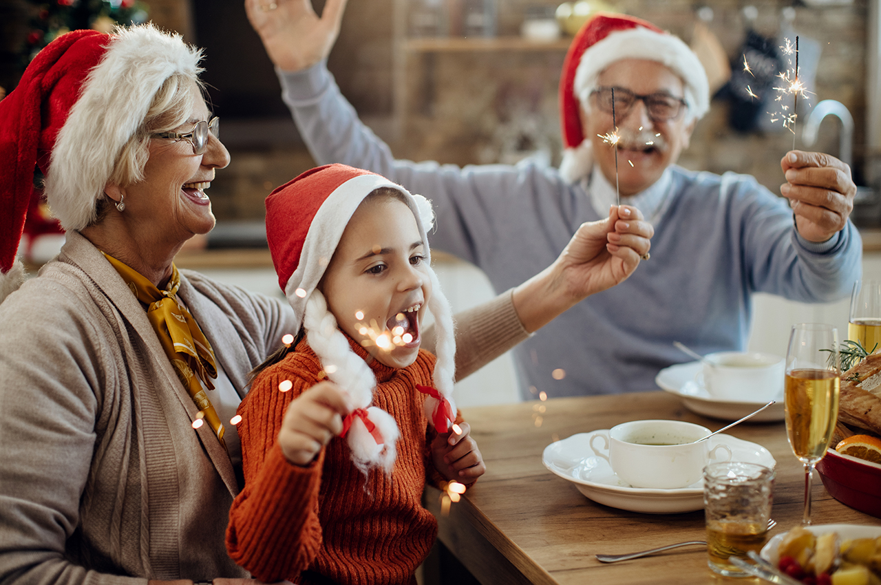 Una nieta y sus abuelos llevan gorros de Navidad y encienden bengalas.