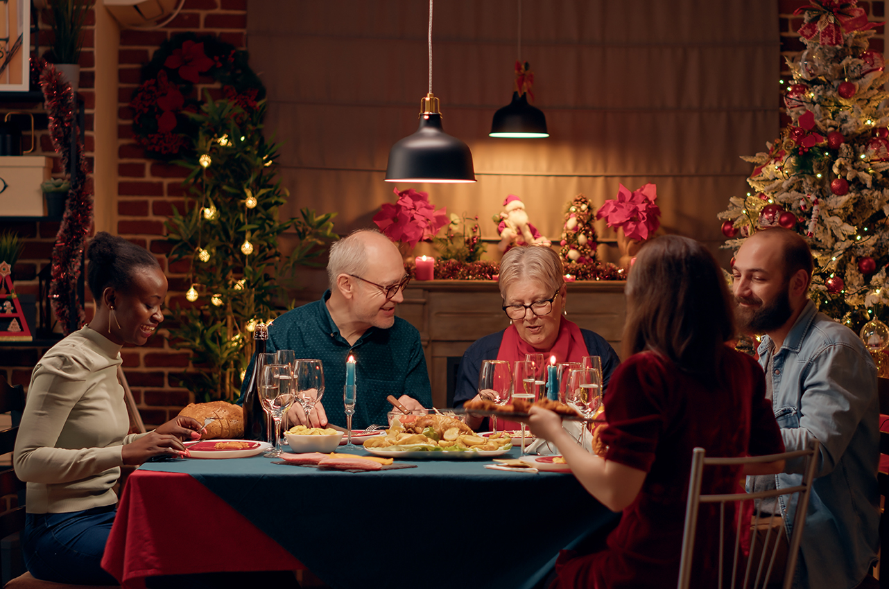 Cinco personas (tres mujeres, una de ellas más mayor; dos hombres, uno de ellos mayor) celebran la cena de Navidad.