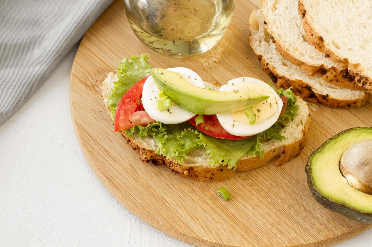 Una tosta con lechuga, tomate, huevo cocido y aguacate.