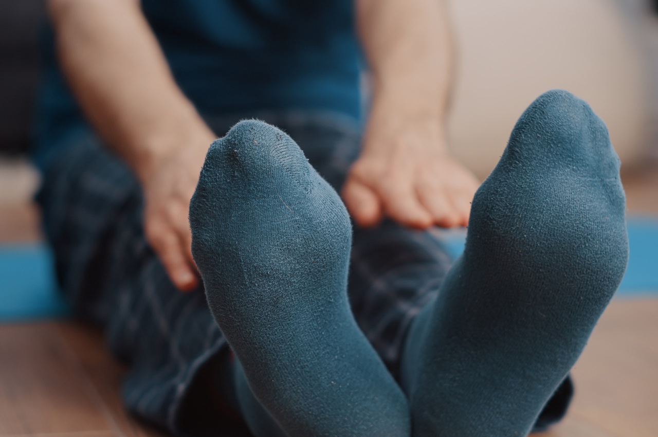 Una persona haciendo estiramientos en el suelo, sentada en una esterilla, tratando de alcanzar la punta de sus pies.