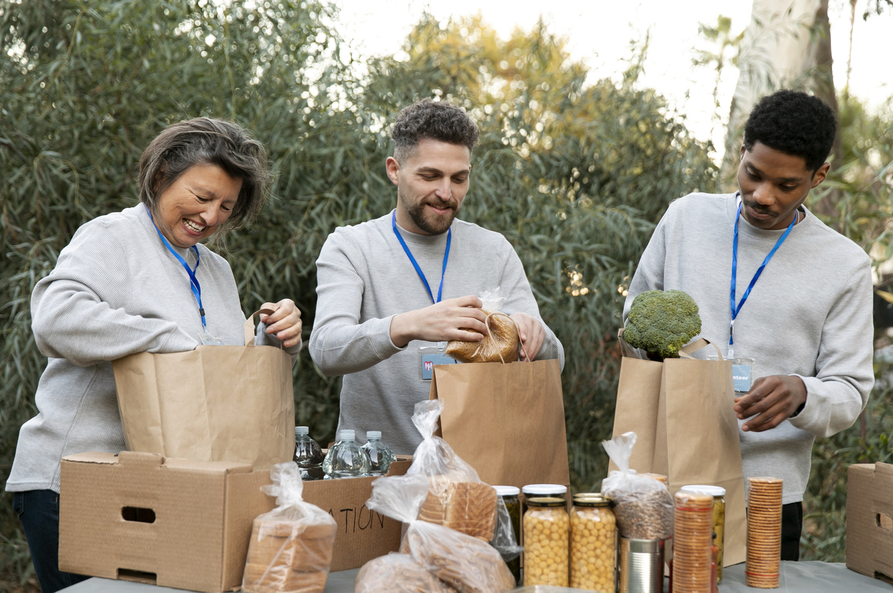 Tres voluntarios (una mujer mayor y dos hombres jóvenes) recogen comida para un banco de alimentos.