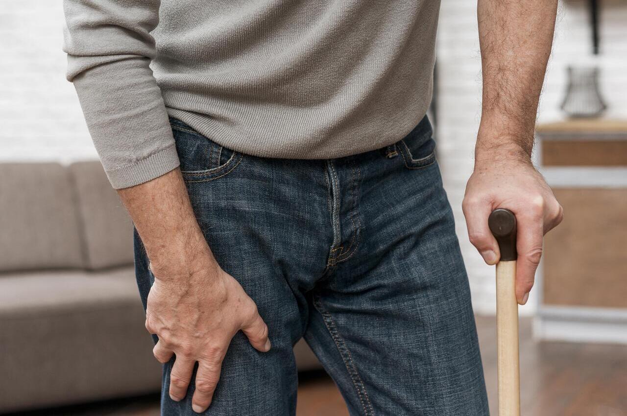 Un hombre aquejado de dolor en la cadera se desplaza ayudado de un bastón.