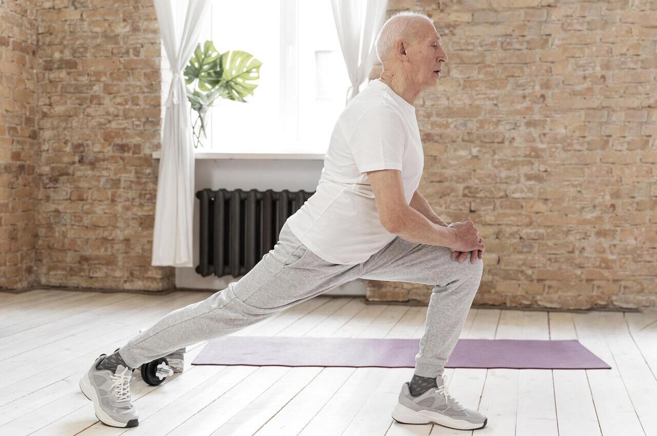 Un hombre mayor realiza estiramientos en su casa.