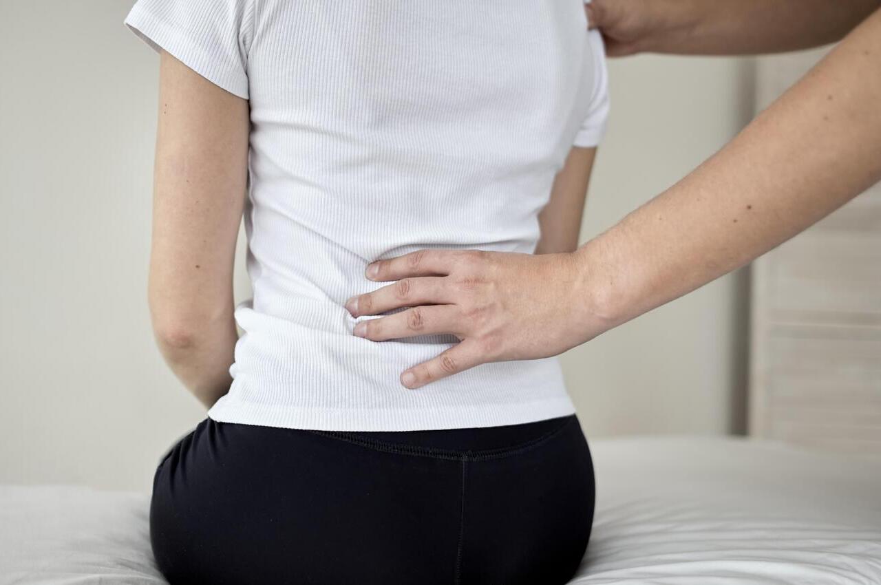 Un profesional de la salud palpando la espalda, a la altura de los riñones, de una paciente.