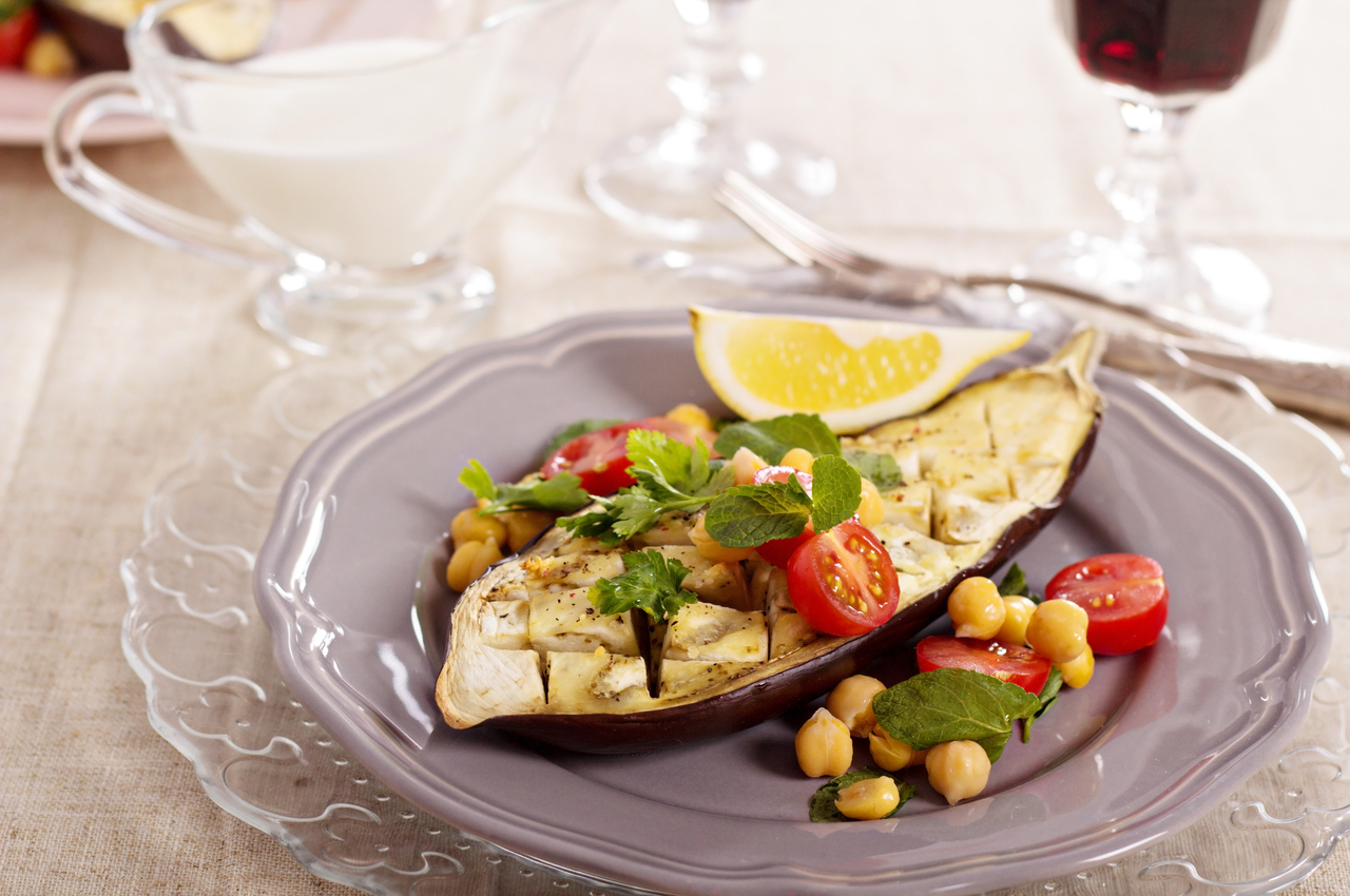 Una berenjena al horno, adornada con garbanzos, tomates y unas hojas de perejil.