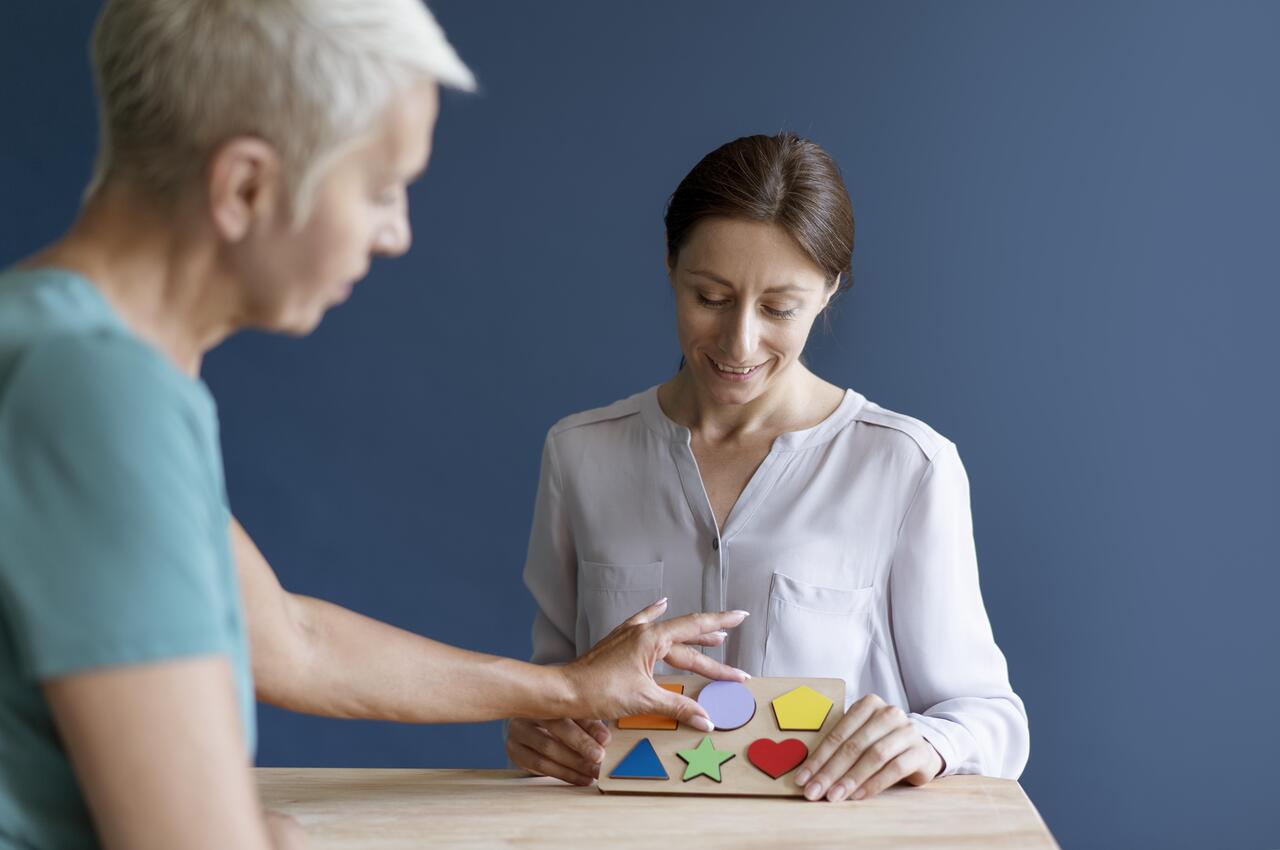 Una mujer mayor realiza un ejercicio de formas y colores en una sesión de terapia ocupacional.