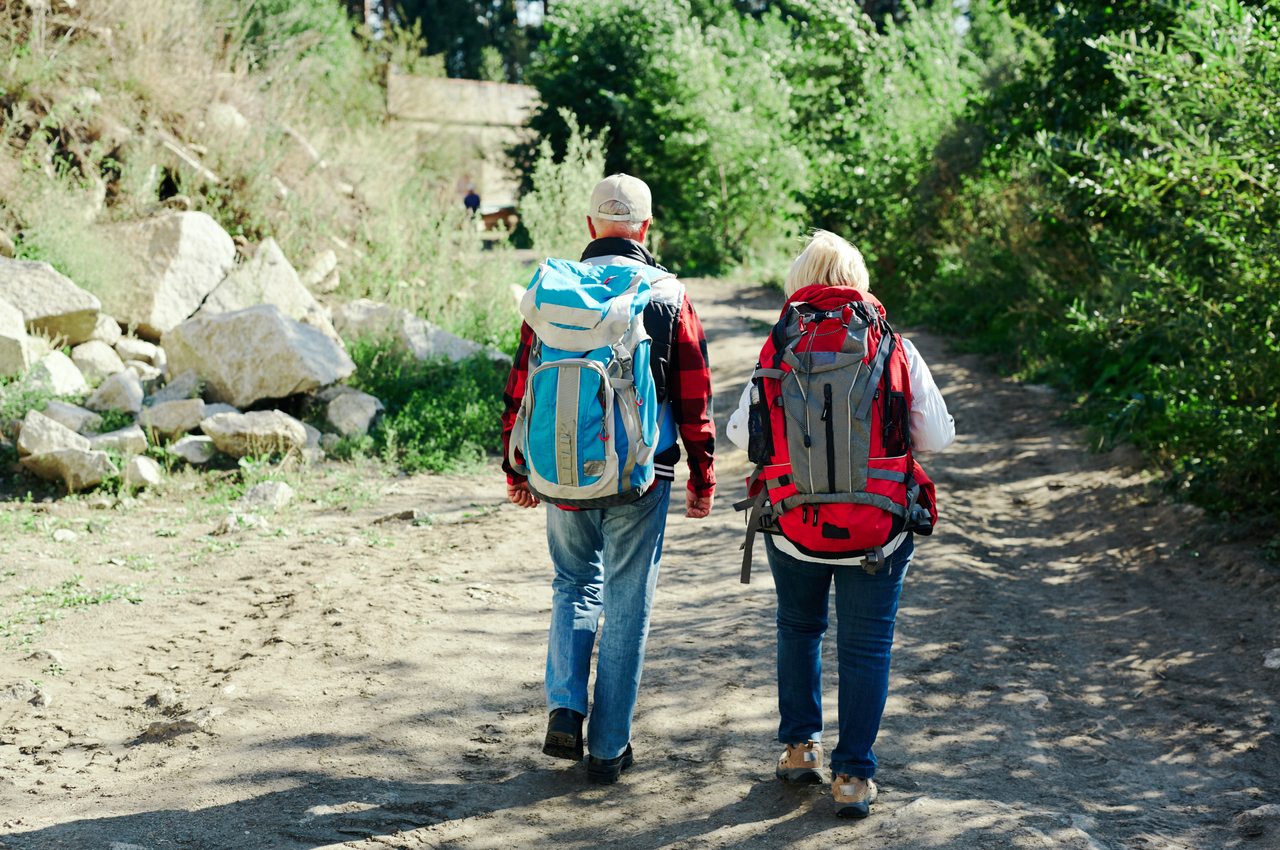 Dos personas mayores equipadas con mochilas durante una caminata en mitad de la naturaleza.
