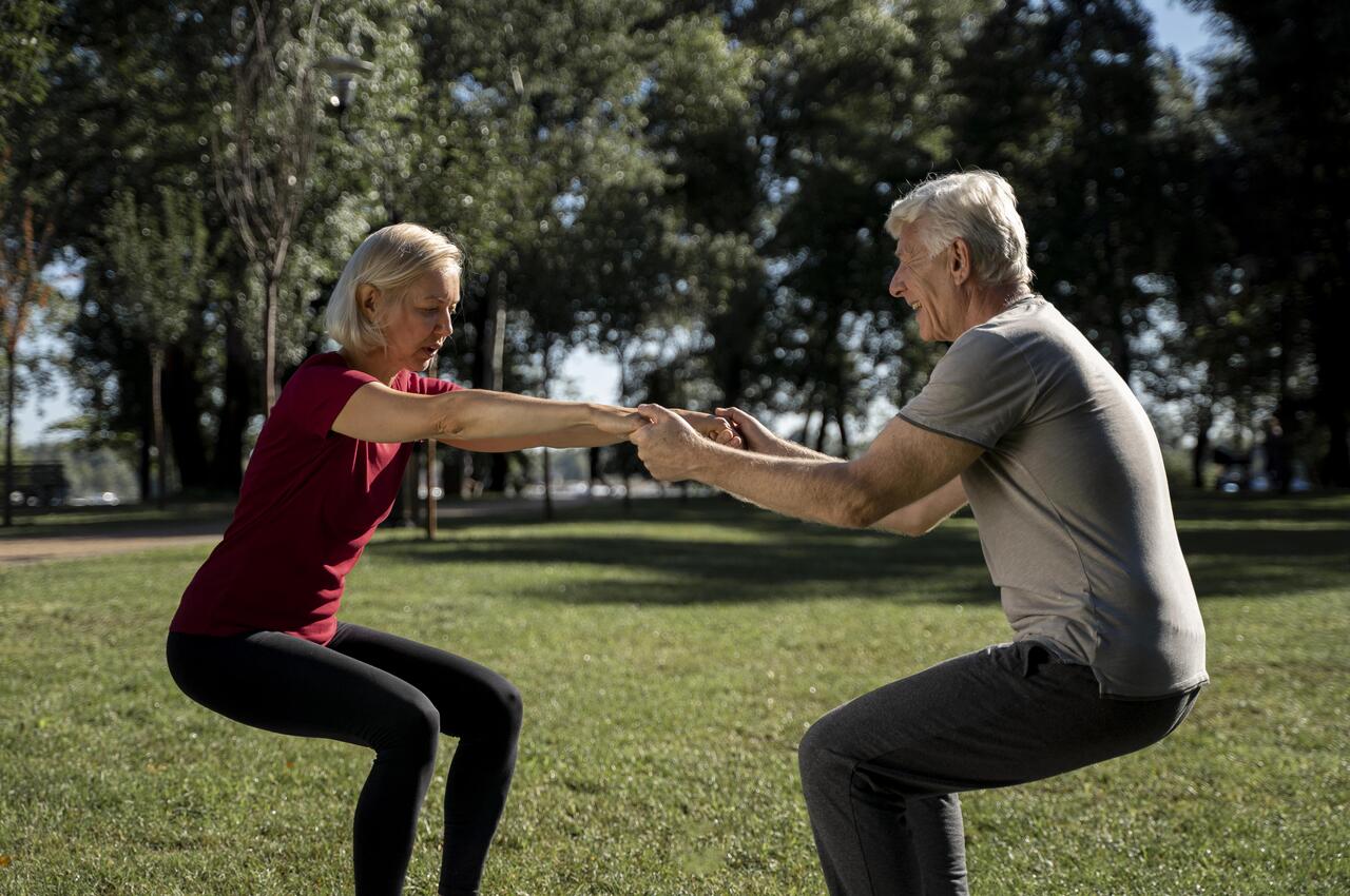 Dos personas mayores hacen ejercicios de equilibrio y resistencia en un parque.