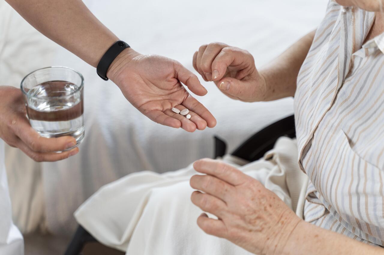 Una persona ofreciendo medicación y un vaso de agua a una mujer mayor.