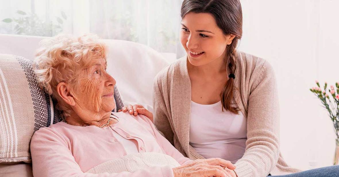 Chica joven cuidando a una mujer mayor con alzhéimer sentada en un sofá
