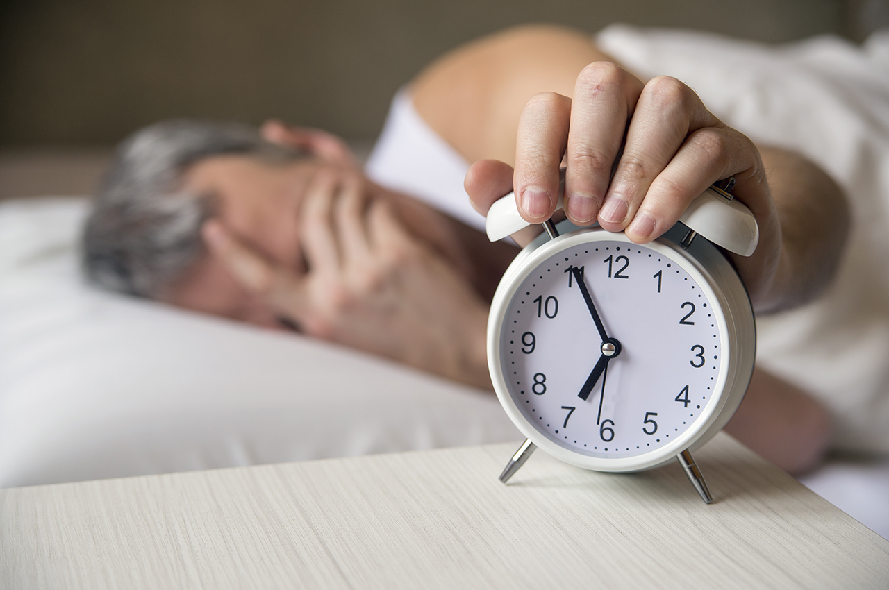 Un hombre mayor apaga la alarma de un reloj.