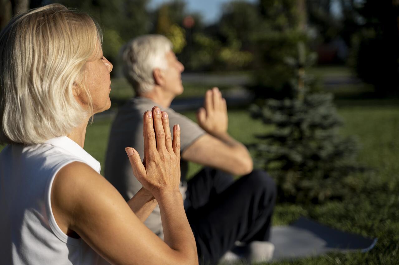 Una pareja de personas mayores practicando respiración consciente en un parque tras haber hecho ejercicio.