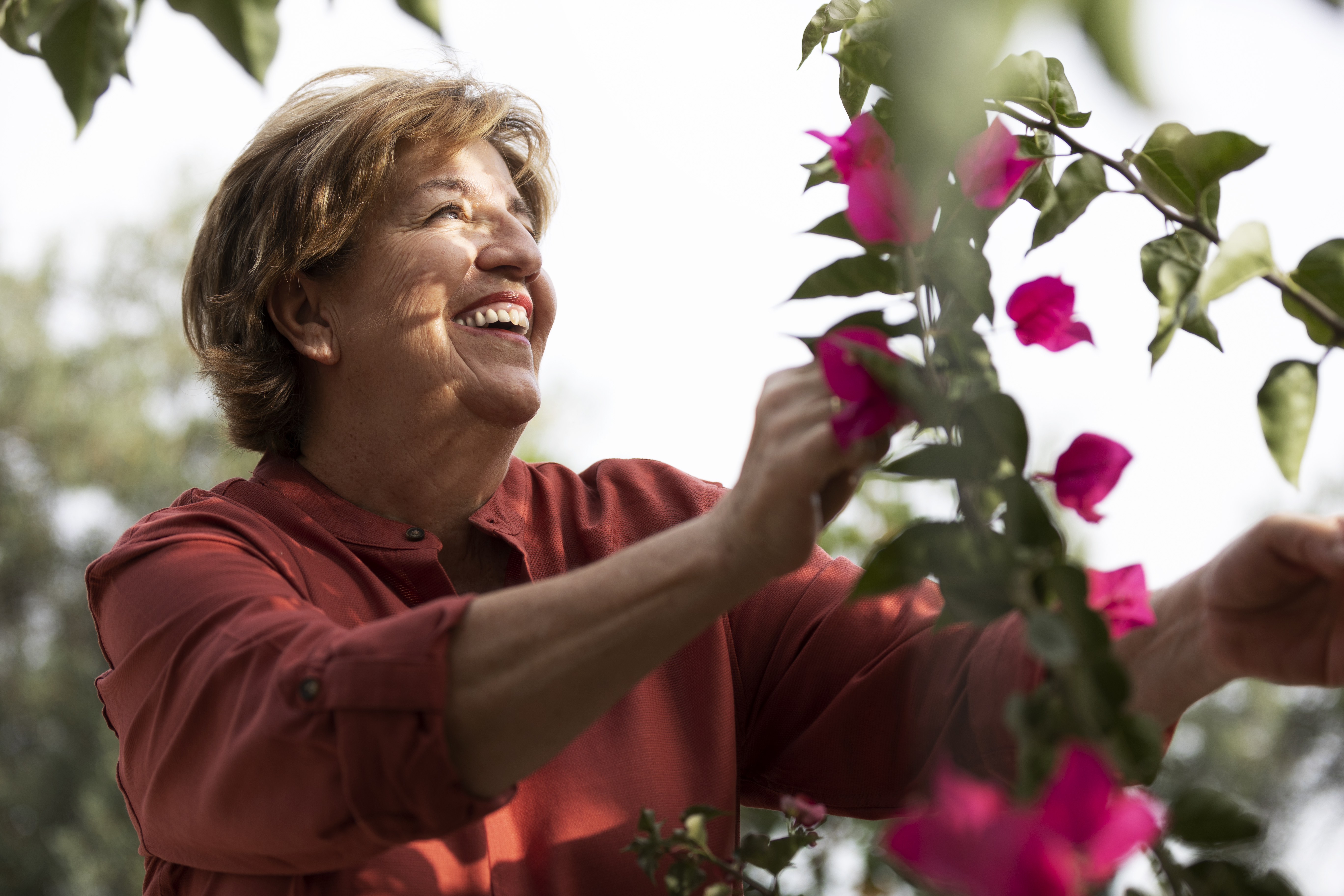 Una mujer mayor cuida de unas flores en un jardín.
