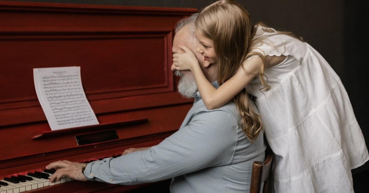 Nieta tapando los ojos de su abuelo que está tocando el piano