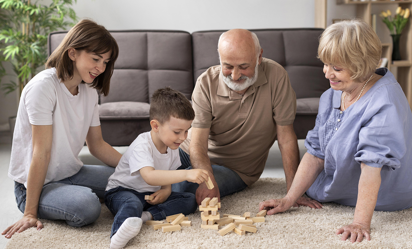 Una familia (abuelo, abuela, madre y niño) jugando al jenga en el salón.
