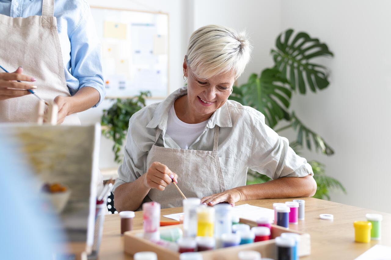 Una mujer mayor sonriente mientras disfruta de un taller de pintura.