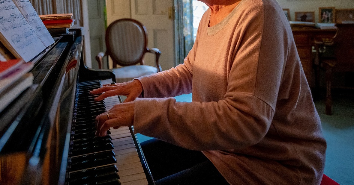 Mujer mayor tocando el piano siguiendo una partitura, una de las actividades que pueden hacerse en la terapia con música para ancianos