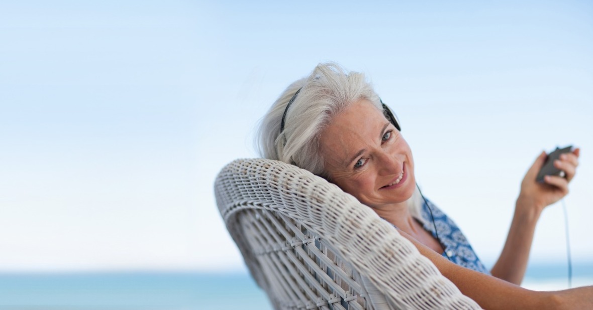 Mujer mayor con aspecto muy saludable escuchando música sentada frente al mar