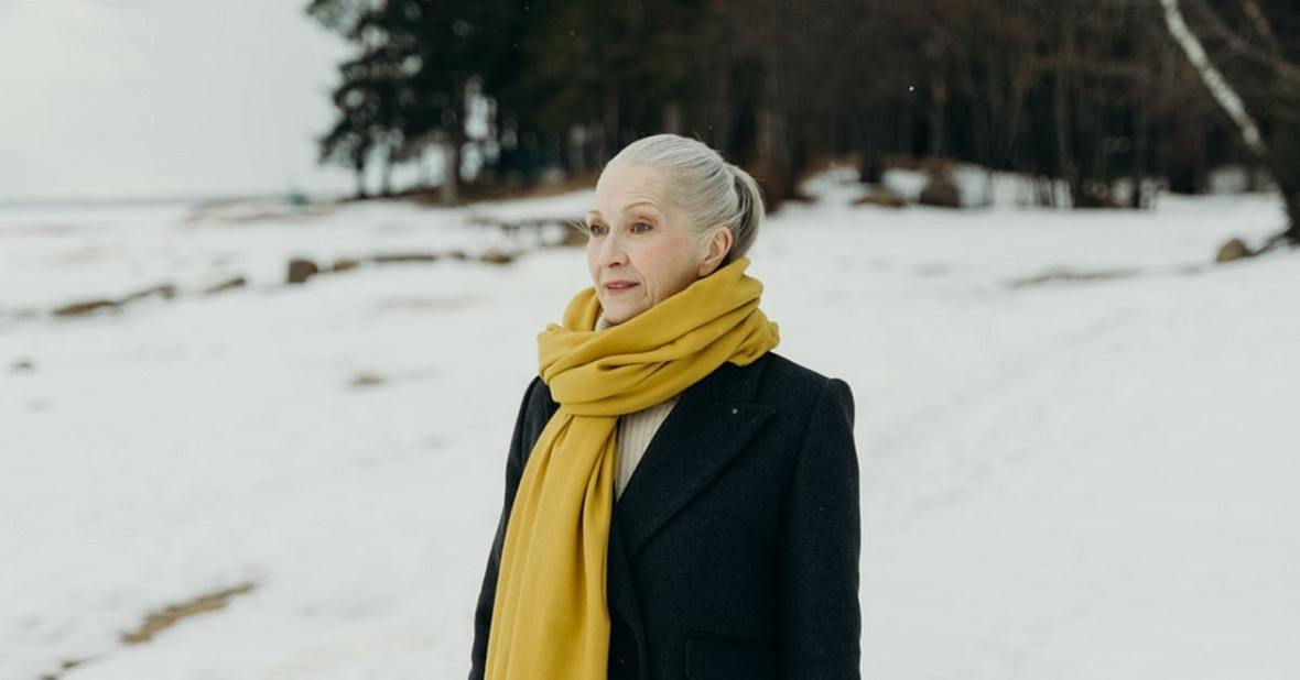 Mujer mayor con abrigo y bufanda en medio de un paisaje nevado