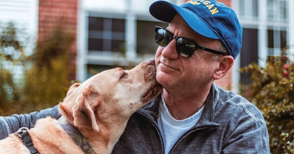 Hombre mayor sonriendo mientras un perro de terapia le lame la mejilla
