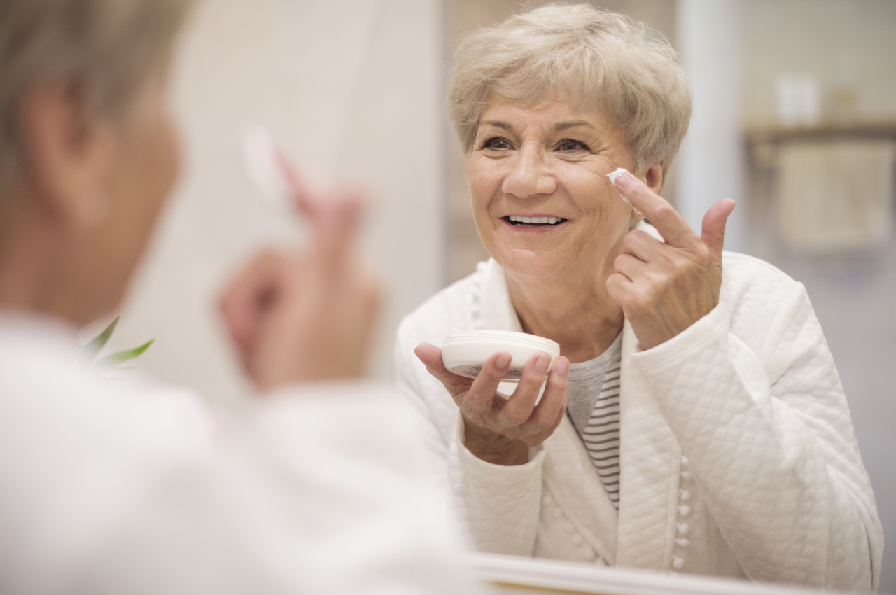 Mujer mayor haciendo una rutina de cuidado de la piel frente al espejo.