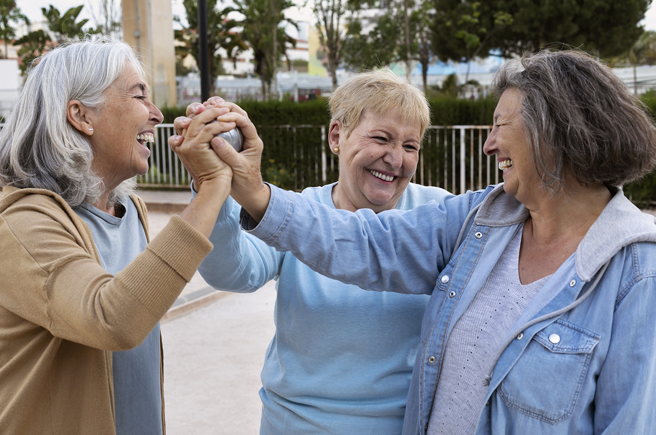 Tres mujeres mayores juegan a la petanca y ríen mientras tanto.