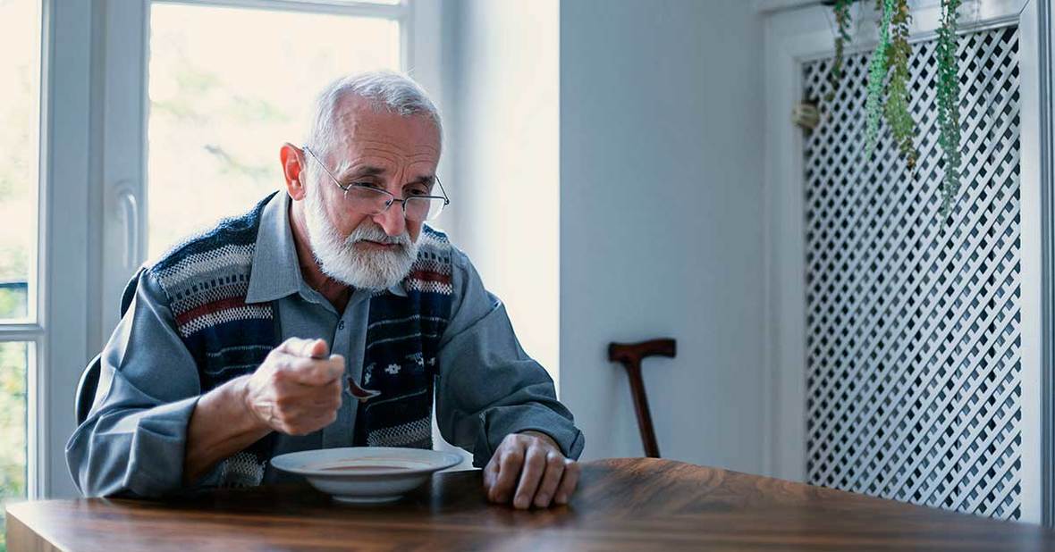 Persona mayor que sufre de hipoxia comiendo un plato de sopa con desgana