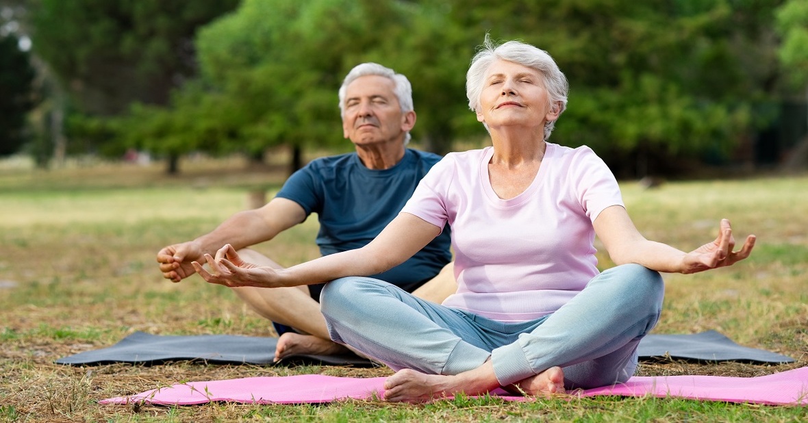 Dos personas mayores haciendo yoga en el parque para obtener los beneficios de realizar actividad física en la tercera edad