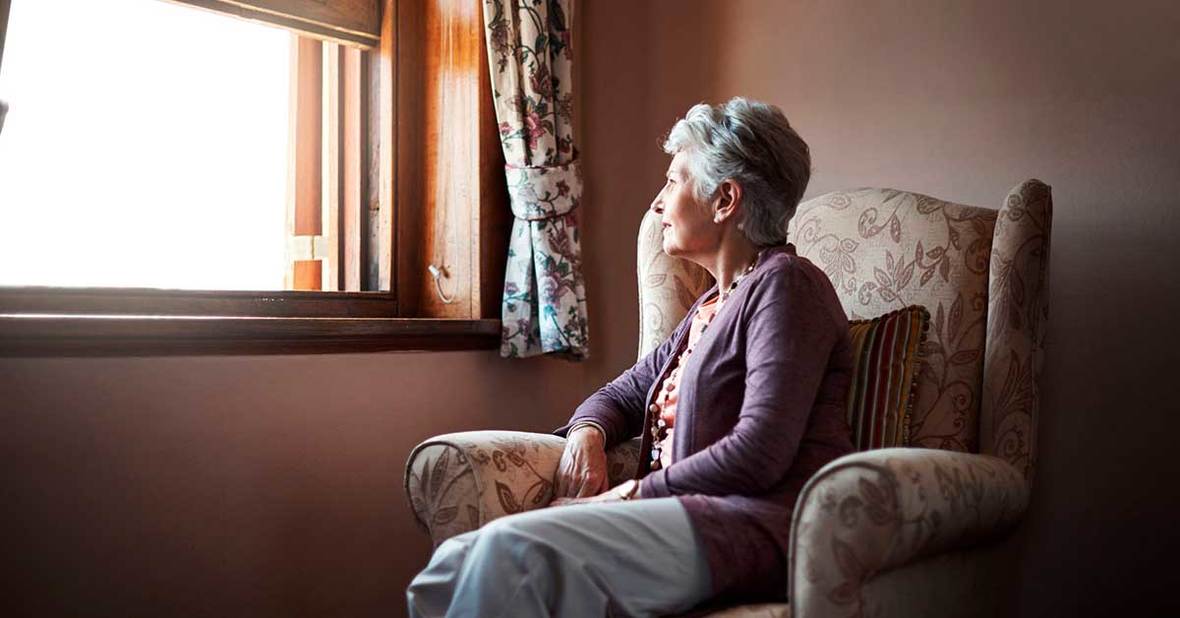 Persona mayor con depresión sentada en un sillón mirando por la ventana de su casa