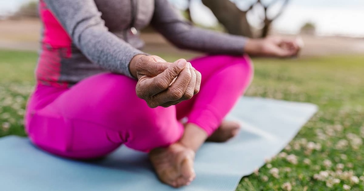 Persona mayor al aire libre practicando yoga, un ejercicio recomendado si se duermen las manos, sentada con las piernas cruzadas sobre una esterilla