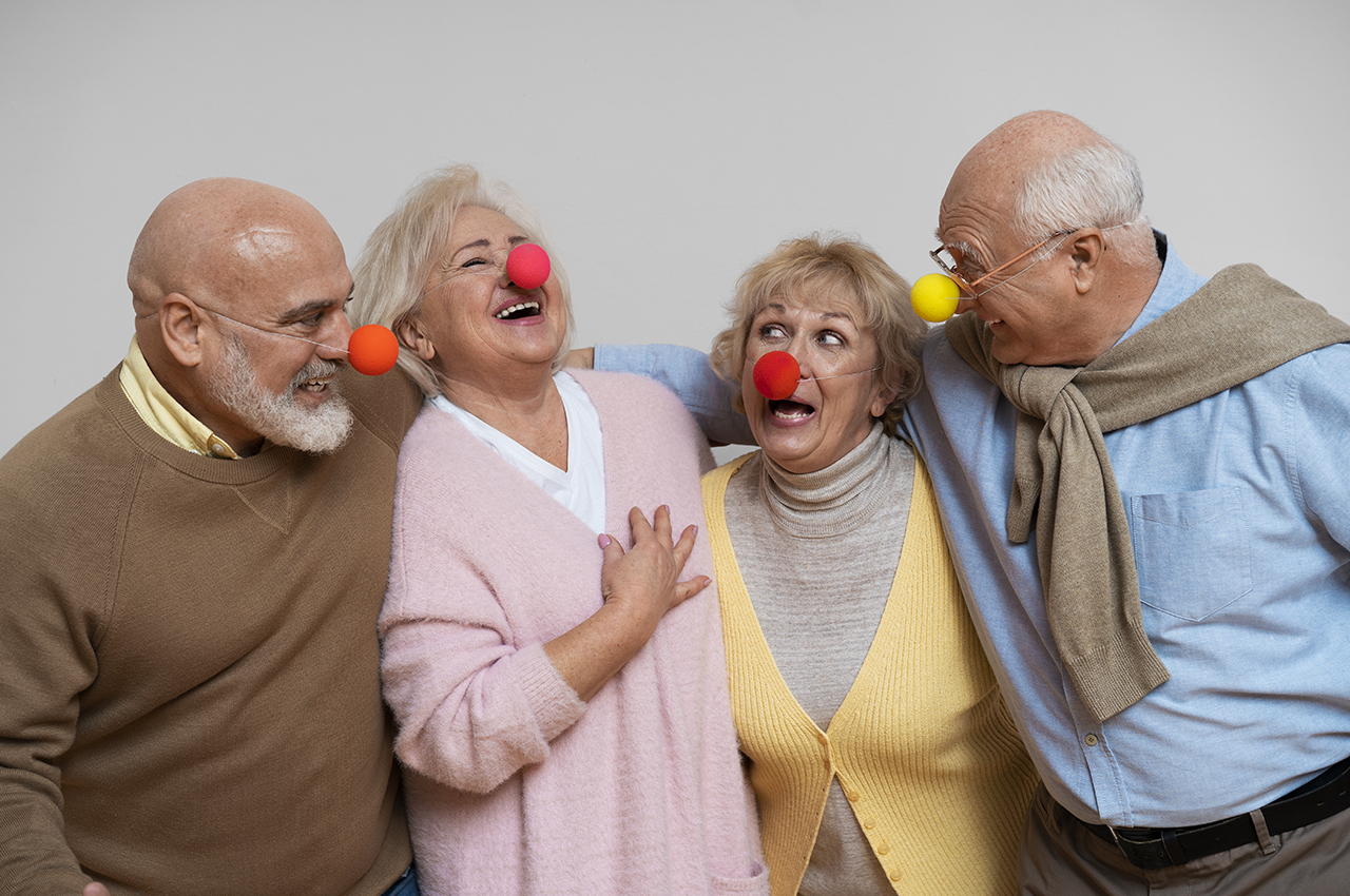 Un grupo de adultos mayores (dos mujeres y dos hombres) riéndose. Todos llevan narices de payaso.