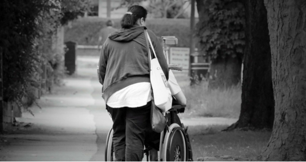 Persona mayor en silla de ruedas paseando con su cuidadora, a la que tiene derecho por la Ley General de la Discapacidad