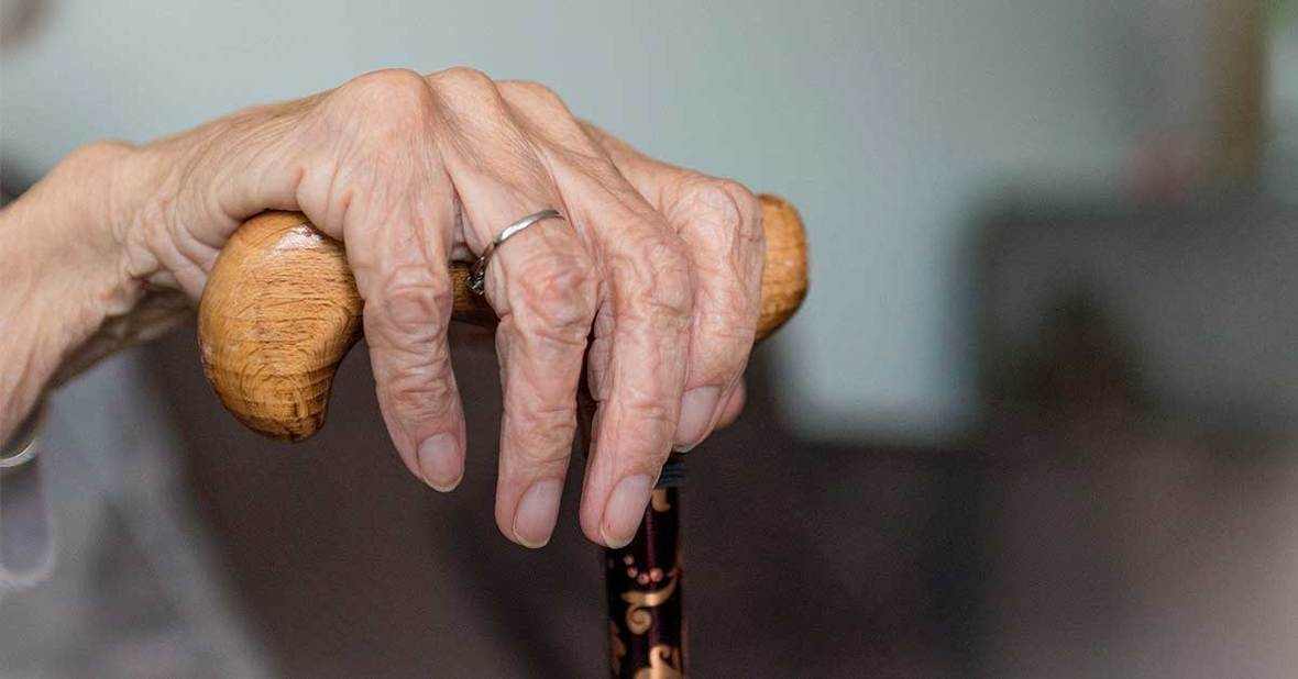 Mano de una mujer mayor sobre un bastón para ayudarse y prevenir caídas típicas en ancianos