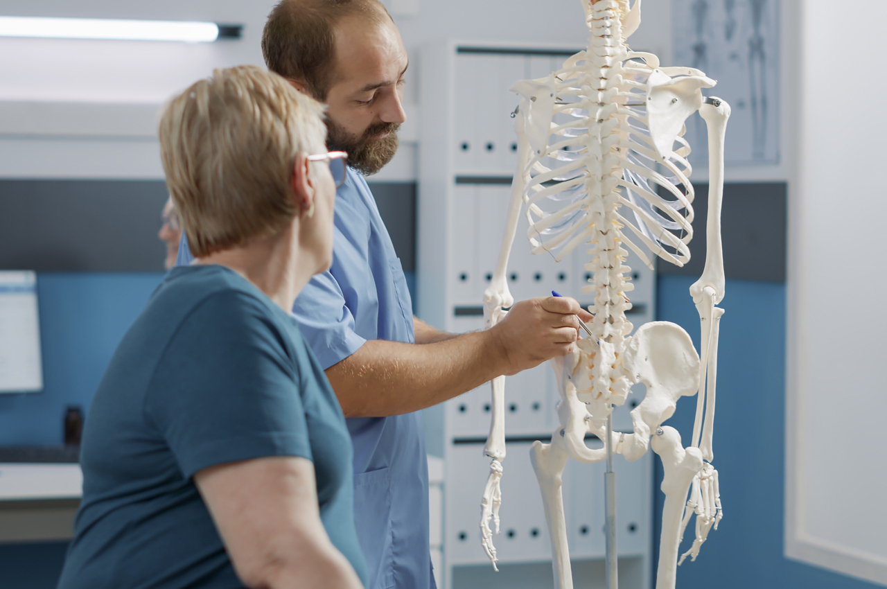 Un médico explica a una mujer mayor las dolencias de la osteoporosis con un esqueleto.