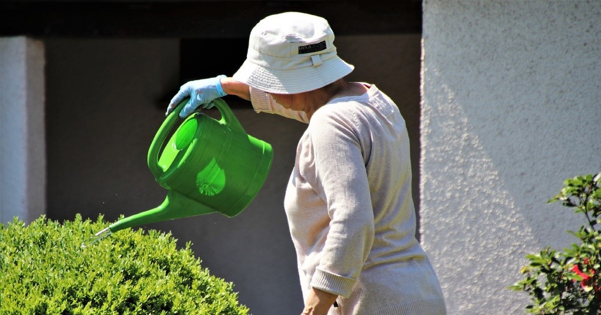 Mujer regando las plantas al aire libre con un gorro en la cabeza como medida de precaución en personas mayores ante el calor